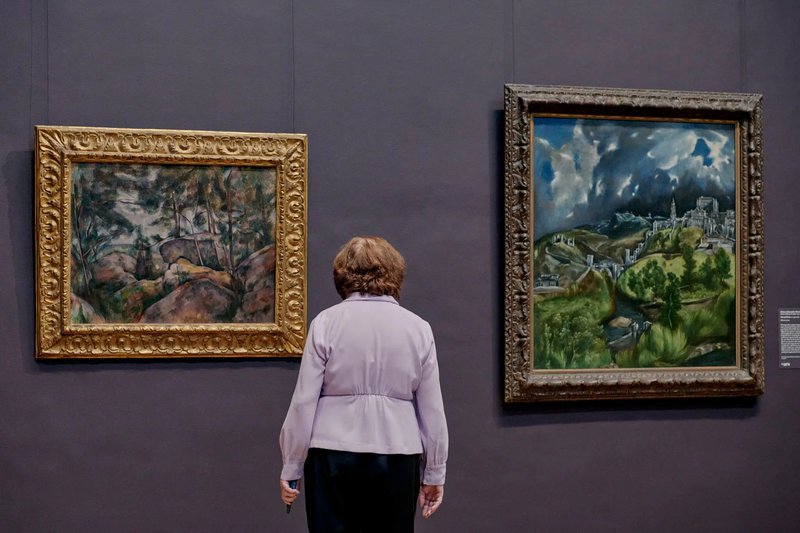 A visitor views “Rocks at Fontainebleau” by Cézanne (left) and “View of Toledo” by El Greco in Gallery 619 in the reinstalled European Paintings wing.